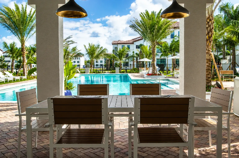Luxury outdoor dining area featuring a faux wood dining set overlooking a resort-style swimming pool and tropical landscaping.